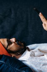 Eine Person liegt auf einem Sofa und schaut in ihr Smartphone.