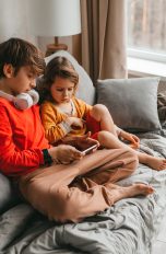 Zwei Kinder sitzen auf einem Sofa und schauen zusammen etwas auf einem Smartphone.