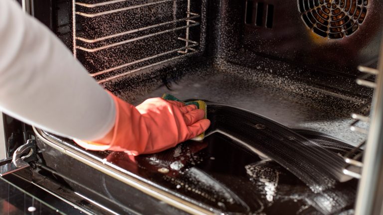 Eine Person trägt Handschuhe und wischt mit einem Schwamm einen Backofen aus.