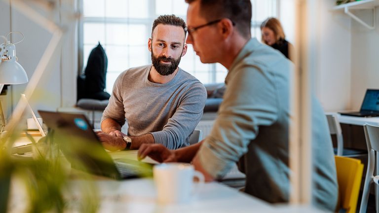 Eine Person zeigt in einem Büro einer anderen Person ihren Laptop-Bildschirm. Eine Person zeigt in einem Büro einer anderen Person ihren Laptop-Bildschirm.