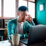 Eine Person sitzt vor einem Laptop und schaut besorgt auf den Bildschirm.