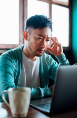 Eine Person sitzt vor einem Laptop und schaut besorgt auf den Bildschirm.