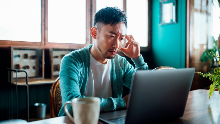 Eine Person sitzt vor einem Laptop und schaut besorgt auf den Bildschirm.