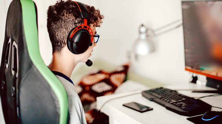 Eine Person mit Headset sitzt vor einem Rechner und schaut in den Bildschirm.