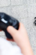 Ein Kind hält eine Fernbedienung in der Hand. Die gehört zu einer Drohne, die vor ihm auf dem Boden steht.