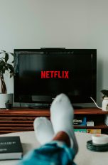 Eine Person hat die Füße auf den Tisch gelegt und schaut auf dem TV Netflix.