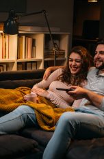 Zwei Personen liegen zusammen auf einem Sofa und schauen TV.