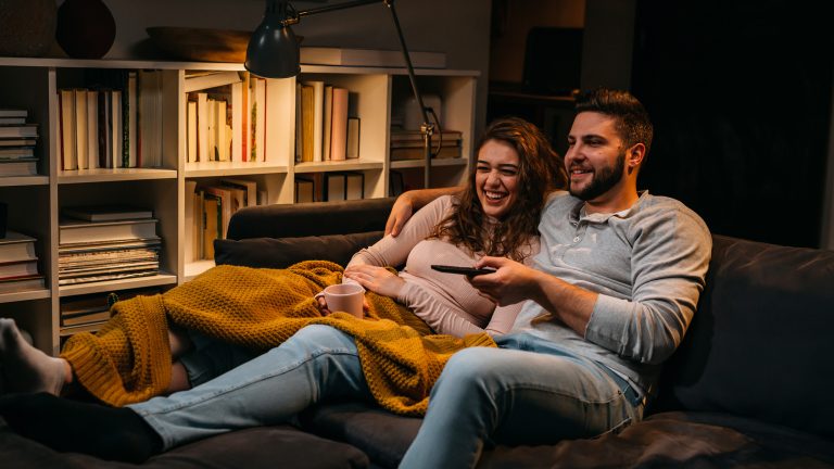 Zwei Personen liegen zusammen auf einem Sofa und schauen TV.