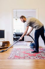 Eine Person saugt mit einem Staubsauger ein Wohnzimmer.
