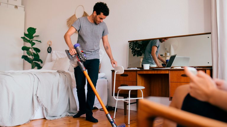 Eine Person saugt mit einem kabellosen Staubsauger ein Schlafzimmer.