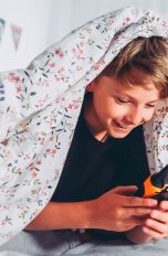 Ein Kind unter einer Bettdecke hält ein Walkie-Talkie in der Hand.