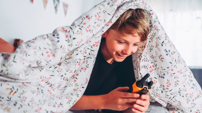 Ein Kind unter einer Bettdecke hält ein Walkie-Talkie in der Hand.