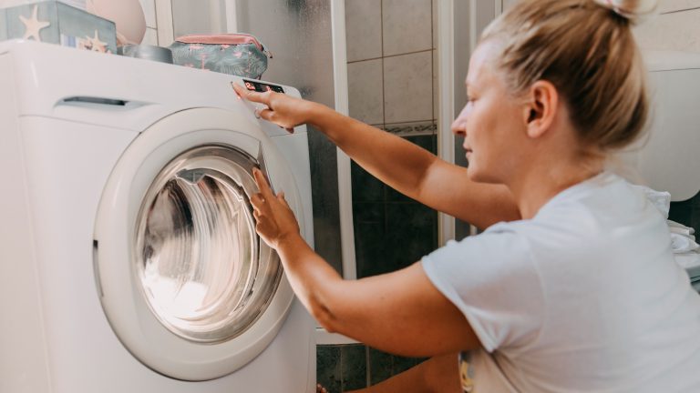 Eine Person sitzt vor einer Waschmaschine und bedient die Knöpfe daran.