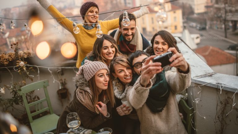 Eine Gruppe Personen in Winterkleidung posiert gemeinsam auf einer Dachterrasse für ein Gruppenselfie.