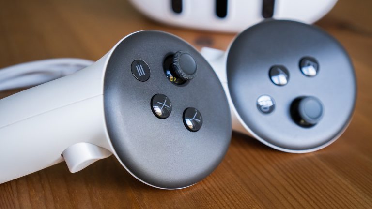 Nahaufnahme der Controller einer Meta Quest 3 mit der VR-Brille im Hintergrund.