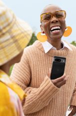 Eine Person hält ein Google Pixel 8 in der Hand und lacht. Neben ihr steht ein Kind.