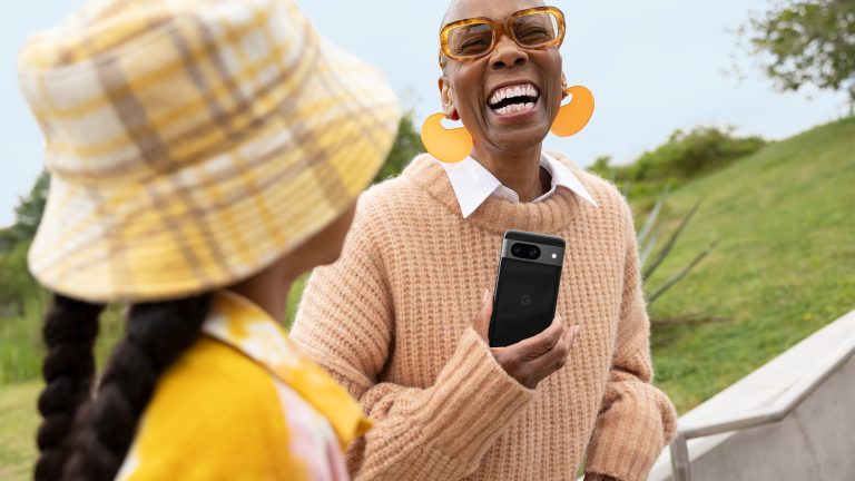 Eine Person hält ein Google Pixel 8 in der Hand und lacht. Neben ihr steht ein Kind.