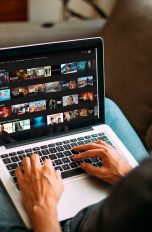 Eine Person sitzt an einem MacBook. Auf dem Display ist die Website von Netflix zu sehen.