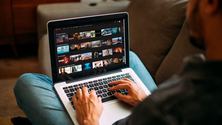 Eine Person sitzt an einem MacBook. Auf dem Display ist die Website von Netflix zu sehen.