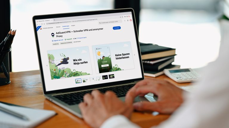 Person vor Laptop auf einem Office-Schreibtisch. Der geöffnete Google Chrome Browser zeigt die Erweiterung „AdGuard VPN“ im „Chrome Web Store“.