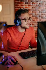 Eine Person mit einem Headset auf dem Kopf sitzt neben einem Gaming-Rechner und scheint etwas zu spielen.