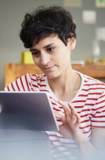 Eine Person sitzt vor einem Tablet und tippt darauf.