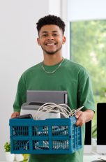 Eine Person trägt einen Korb voller Elektroschrott aus einem Büro heraus.