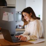 Eine Person steht in einer Küche und arbeitet an einem MacBook.