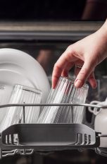 Eine Hand stellt ein Glas neben andere Gläser und eine Schüssel in das obere Fach eines Geschirrspülers.