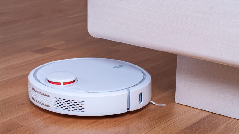 Ein weißer, flacher, runder Wischroboter steht neben einer Möbelkante.