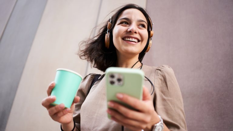 Eine Person hält ein iPhone in der Hand und hört auf angeschlossenen Kopfhörern etwas.
