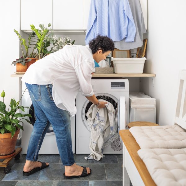 Eine Person packt ein wenig Wäsche in eine Waschmaschine, die in einem Waschraum steht.