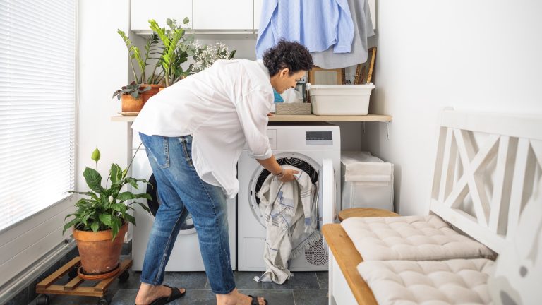 Eine Person packt ein wenig Wäsche in eine Waschmaschine, die in einem Waschraum steht.