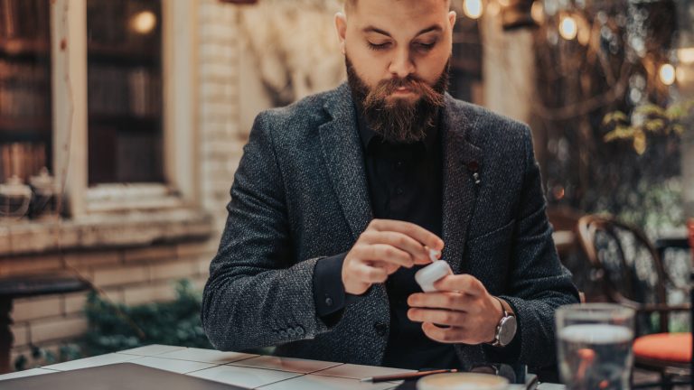 Eine Person sitzt in einem Café und steckt ihre AirPods wieder in das Case.