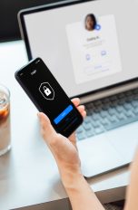 Eine Person mit Smartphone und Laptop, die eine 2-Faktor-Authentifizierung durchführt.