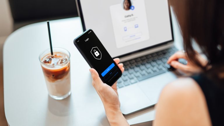 Eine Person mit Smartphone und Laptop, die eine 2-Faktor-Authentifizierung durchführt.