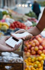 Eine Person hält ihr iPhone an ein Kartenlesegerät um etwas per Apple Pay zu bezahlen.