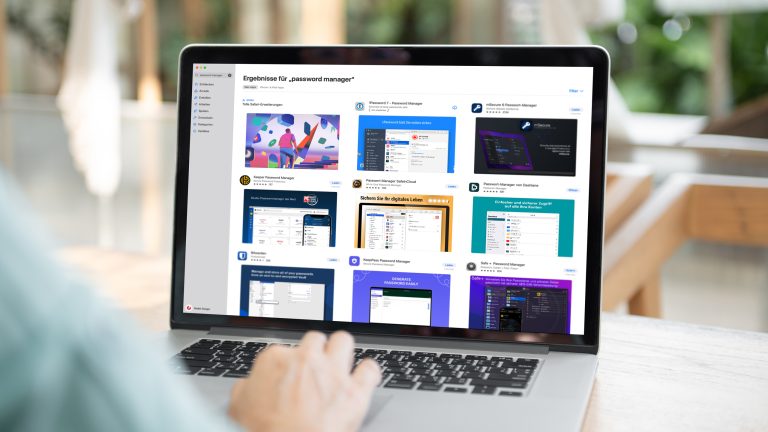 Person sitzt mit einem MacBook im Freien. Auf dem Bildschirm ist der Apple Appstore mit einer Übersicht von Passwort-Managern geöffnet.