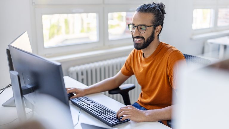 Eine Person sitzt in einem Büro vor zwei Monitoren.