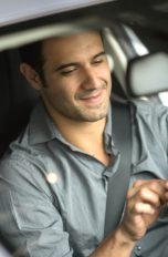 Eine Person sitzt im geparkten Auto und bedient ein Smartphone.