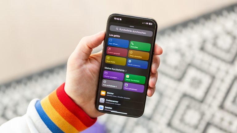 Eine Person hält ein iPhone 15 Pro. Darauf zu sehen ist die На главную der Kurzbefehle-App. Eine Person hält ein iPhone 15 Pro. Darauf zu sehen ist die На главную der Kurzbefehle-App.