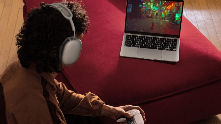 Eine Person hockt vor einem MacBook Air und hält dabei einen Controller in der Hand. Auf dem MacBook läuft ein Spiel.