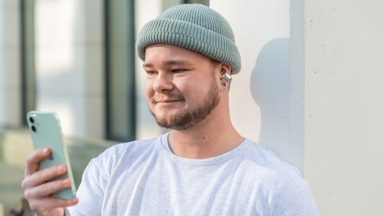 Bose Ultra Open Earbuds Eine Person trägt die Ultra Open Earbuds von Bose und schaut auf ein iPhone.