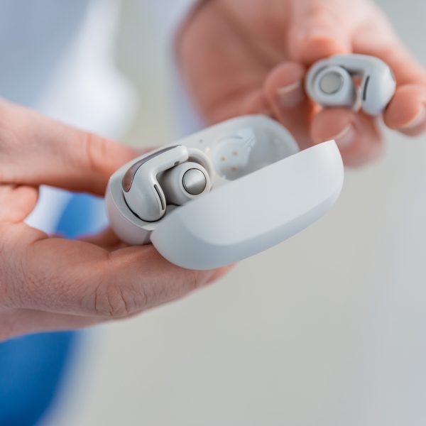 Eine Person hält die Bose Ultra Open Earbuds in Weiß in der Hand.