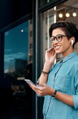 Eine Person trägt AirPods im Ohr und hält ein Smartphone in der Hand.