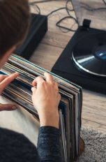 Eine Person sitzt vor einem Plattenspieler und sucht aus einer Reihe von Schallplatten eine aus.