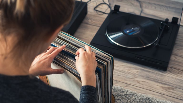 Eine Person sitzt vor einem Plattenspieler und sucht aus einer Reihe von Schallplatten eine aus.