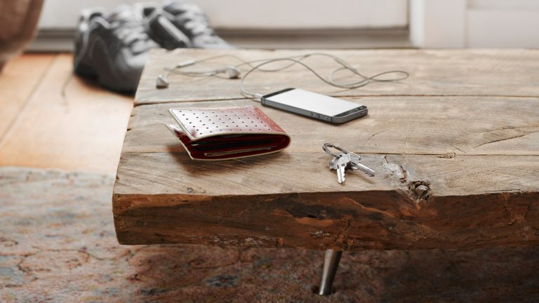 Die tägliche Routine verlassen, ohne etwas zu vergessen – Tracker sorgen für mehr Sicherheit Sitzbank vor einem Hauseingang auf der ein Telefon, Schlüssel und eine Brieftasche liegen.