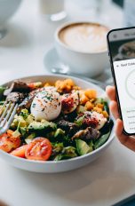 Eine Person sitzt vor einer Bowl und hält ein Smartphone in der Hand.