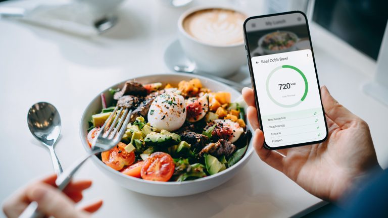 Eine Person sitzt vor einer Bowl und hält ein Smartphone in der Hand.